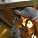 A worker fixing pipes with tools in an industrial indoor environment.